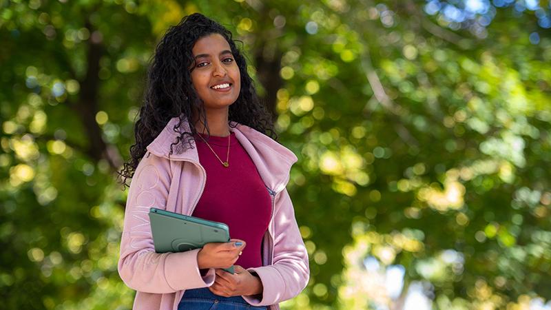 Student with iPad smiling outside